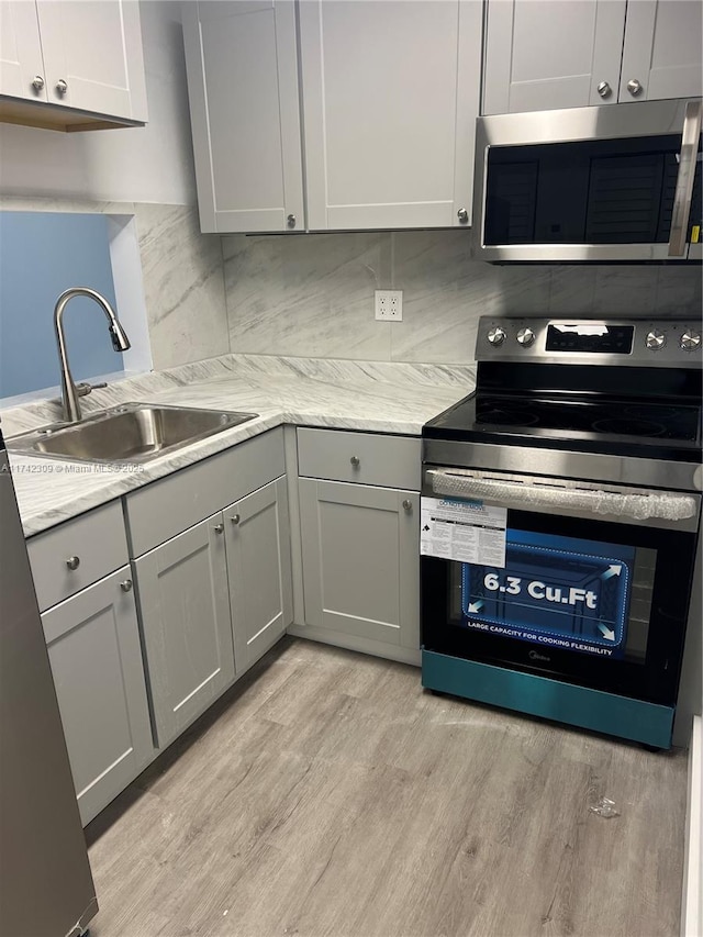 kitchen with appliances with stainless steel finishes, tasteful backsplash, sink, gray cabinetry, and light hardwood / wood-style floors