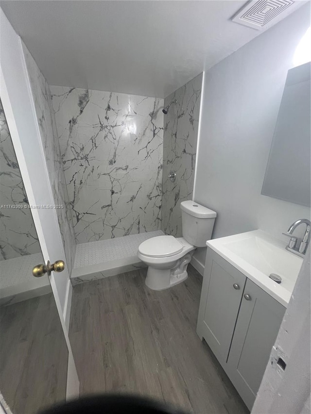 bathroom featuring tiled shower, vanity, toilet, and hardwood / wood-style floors