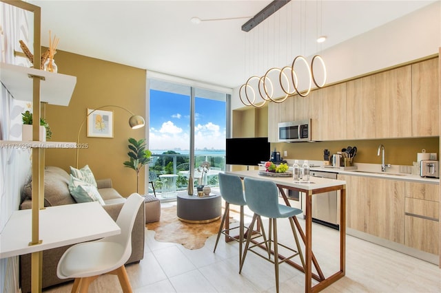 kitchen with sink, stainless steel appliances, floor to ceiling windows, decorative light fixtures, and light brown cabinets