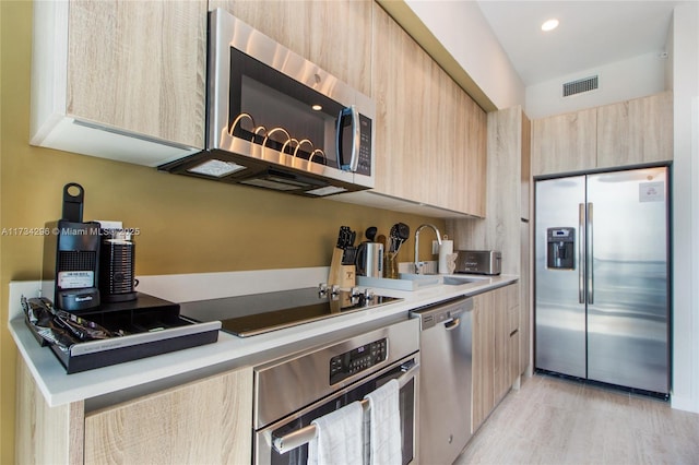 kitchen with appliances with stainless steel finishes, sink, light brown cabinets, and light hardwood / wood-style flooring