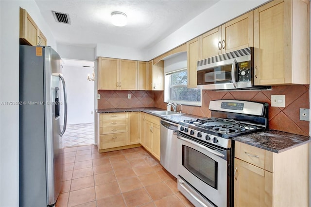 kitchen featuring appliances with stainless steel finishes, sink, dark stone countertops, and light brown cabinetry