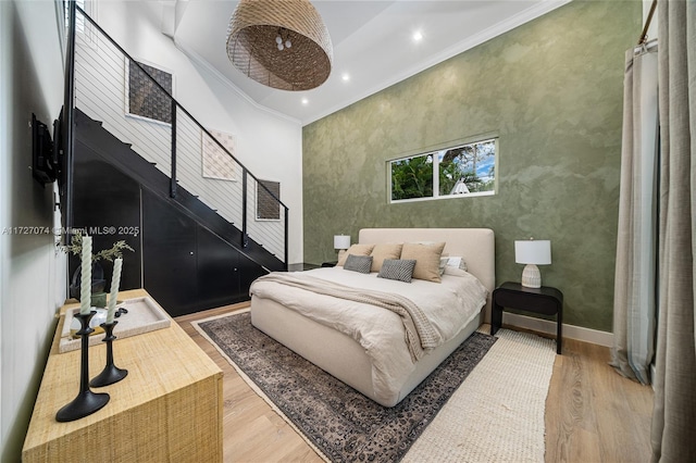 bedroom with baseboards, a high ceiling, ornamental molding, and wood finished floors