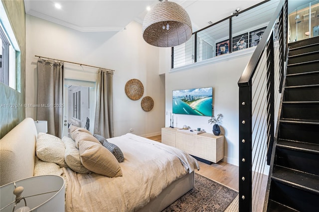 bedroom with baseboards, a high ceiling, ornamental molding, and wood finished floors