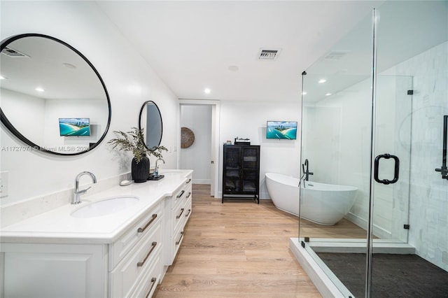 bathroom with double vanity, visible vents, a soaking tub, wood finished floors, and a sink