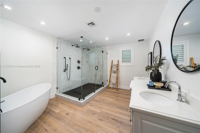 bathroom featuring wood finished floors, a sink, visible vents, a freestanding bath, and double vanity