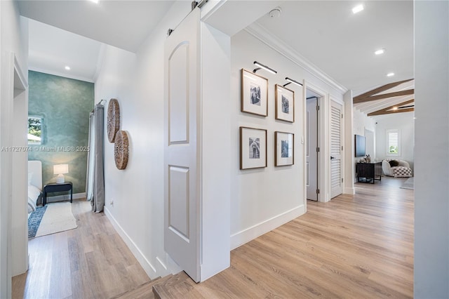 hall featuring a barn door, light wood-style flooring, recessed lighting, baseboards, and crown molding