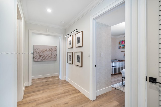 hallway featuring baseboards, crown molding, and light wood finished floors