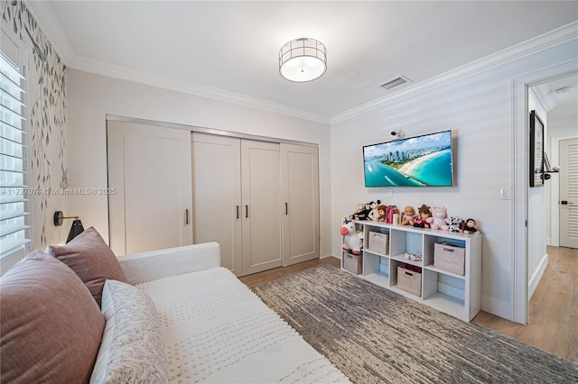 bedroom with visible vents, baseboards, ornamental molding, light wood-style floors, and a closet