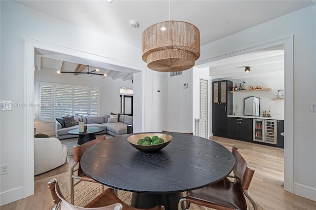 dining room with wine cooler, beam ceiling, light wood-style floors, a bar, and baseboards