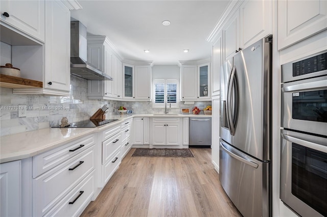 kitchen featuring a sink, white cabinets, light countertops, appliances with stainless steel finishes, and wall chimney range hood