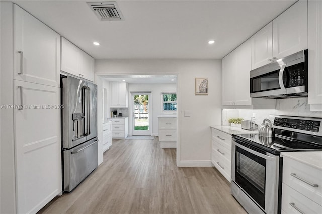 kitchen with appliances with stainless steel finishes, white cabinets, light wood-type flooring, and decorative backsplash