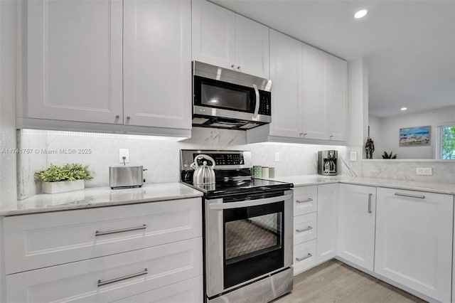 kitchen featuring white cabinets, decorative backsplash, stainless steel appliances, light stone countertops, and light wood-type flooring