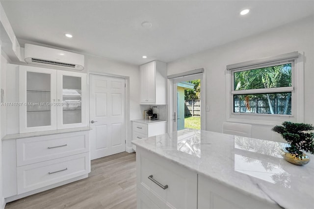 kitchen featuring white cabinetry, light stone countertops, light hardwood / wood-style flooring, and a wall unit AC