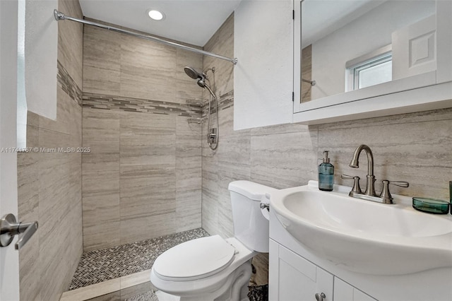 bathroom featuring tiled shower, vanity, toilet, and tile walls