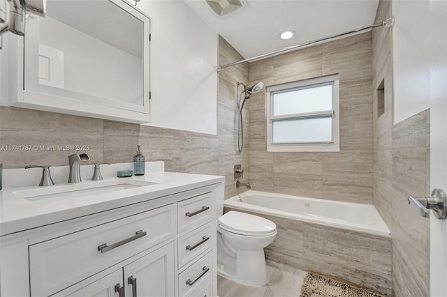 full bathroom featuring tiled shower / bath, vanity, toilet, and tile walls