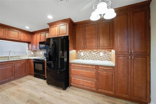 kitchen featuring sink, tasteful backsplash, light stone counters, black appliances, and light wood-type flooring