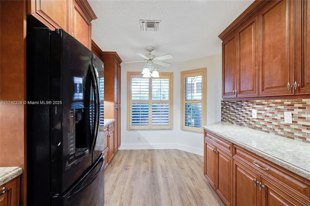 kitchen with light wood-type flooring, backsplash, light stone counters, black fridge with ice dispenser, and a textured ceiling