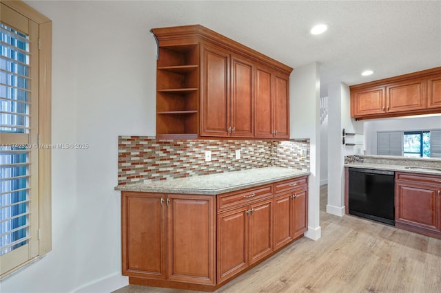 kitchen featuring dishwasher, light stone countertops, backsplash, and light wood-type flooring