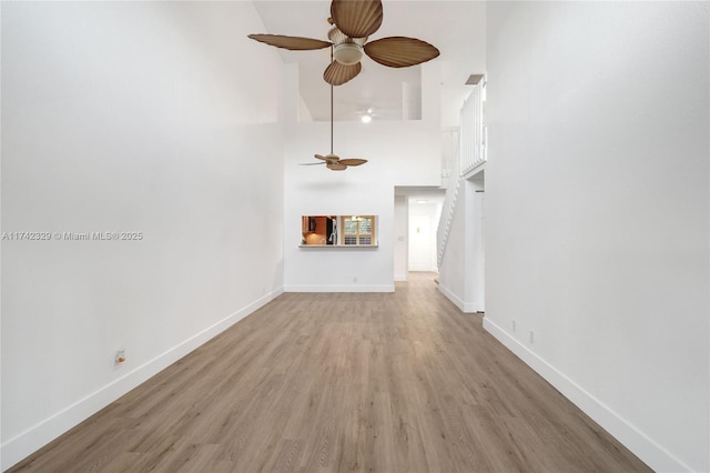 unfurnished living room with ceiling fan, a high ceiling, and light wood-type flooring