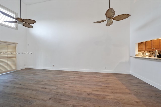 unfurnished living room featuring hardwood / wood-style floors, ceiling fan, and a high ceiling