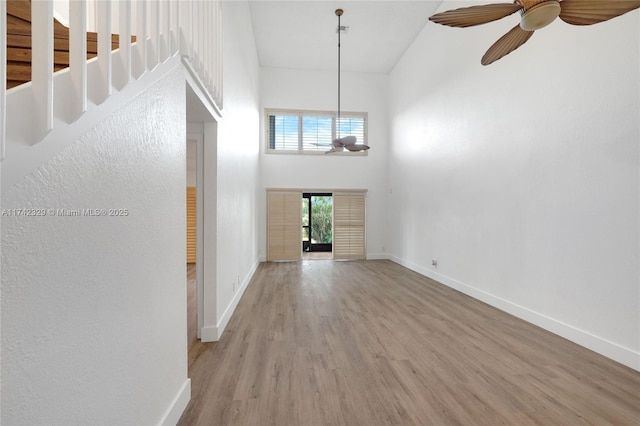 unfurnished living room featuring ceiling fan, light hardwood / wood-style flooring, and a high ceiling