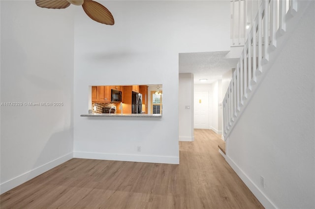 unfurnished living room with ceiling fan, a high ceiling, and light wood-type flooring