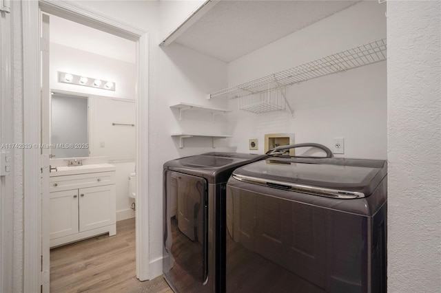 clothes washing area with sink, independent washer and dryer, and light wood-type flooring