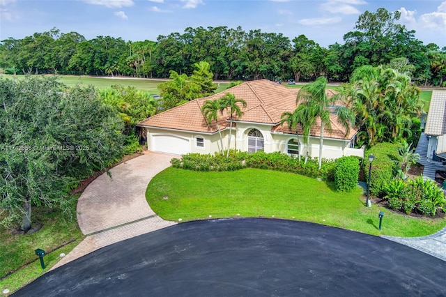 mediterranean / spanish house with decorative driveway, stucco siding, an attached garage, a front yard, and a tiled roof