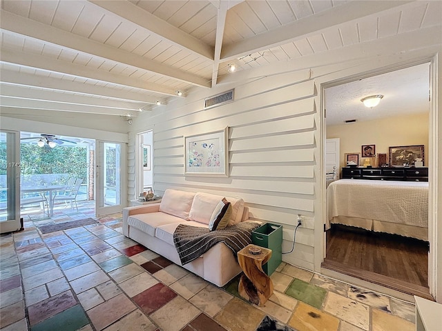 living area featuring beamed ceiling, ceiling fan, visible vents, wooden ceiling, and stone tile flooring