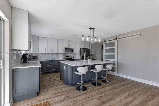 kitchen with decorative light fixtures, a center island with sink, gray cabinets, stainless steel appliances, and a barn door