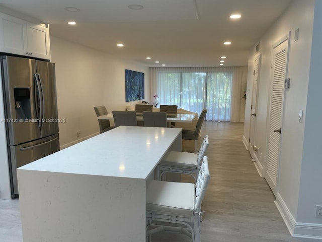 kitchen featuring a kitchen bar, white cabinetry, a center island, light wood-type flooring, and stainless steel fridge