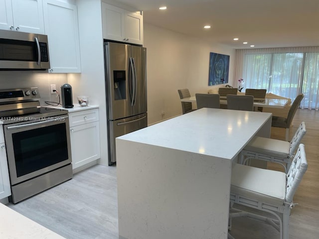 kitchen featuring a breakfast bar area, white cabinetry, a center island, light hardwood / wood-style flooring, and stainless steel appliances