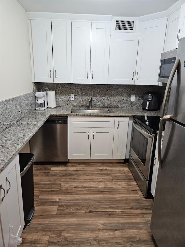 kitchen with appliances with stainless steel finishes, dark hardwood / wood-style floors, white cabinetry, sink, and light stone countertops