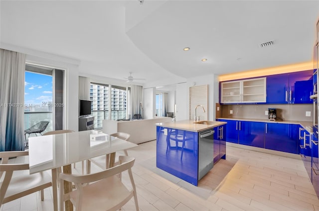 kitchen featuring dishwasher, sink, ceiling fan, blue cabinetry, and a center island with sink