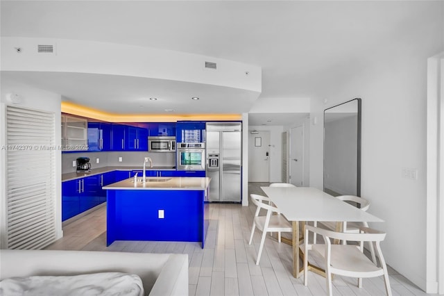 kitchen with blue cabinetry, sink, an island with sink, stainless steel appliances, and light hardwood / wood-style floors