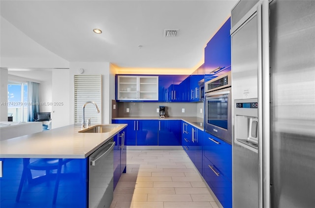 kitchen with blue cabinetry, appliances with stainless steel finishes, sink, and a center island with sink