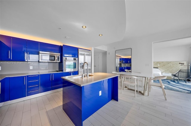 kitchen with sink, a center island with sink, light hardwood / wood-style floors, and appliances with stainless steel finishes