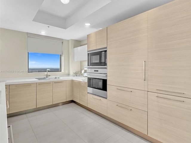 kitchen with light brown cabinetry, oven, sink, and black microwave