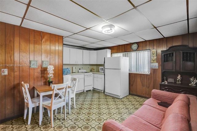 kitchen featuring a drop ceiling, white cabinets, white appliances, and wood walls