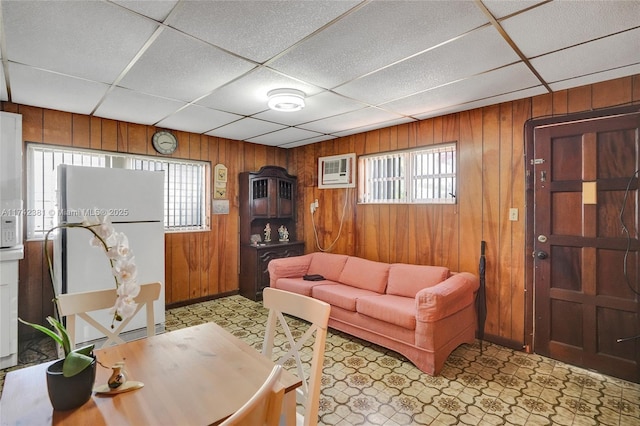 living room featuring a drop ceiling, a wall unit AC, and wood walls