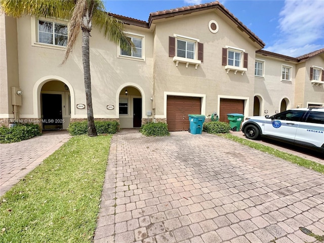 mediterranean / spanish-style house featuring a tiled roof, a garage, stucco siding, and decorative driveway