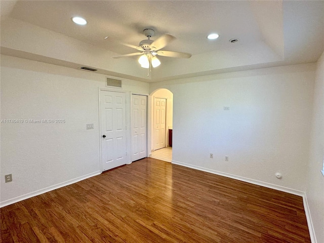 unfurnished bedroom with arched walkways, wood finished floors, baseboards, and visible vents