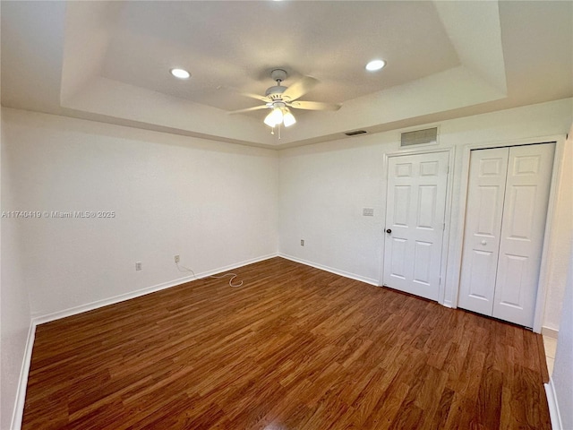 unfurnished bedroom with a raised ceiling, baseboards, and dark wood finished floors