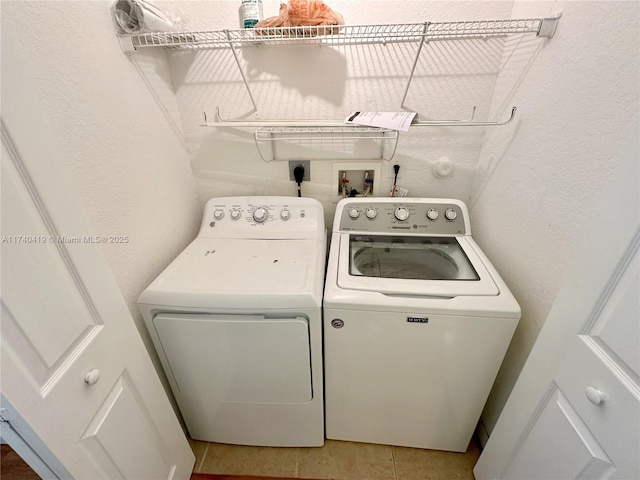 laundry room with light tile patterned floors, washing machine and clothes dryer, a textured wall, and laundry area