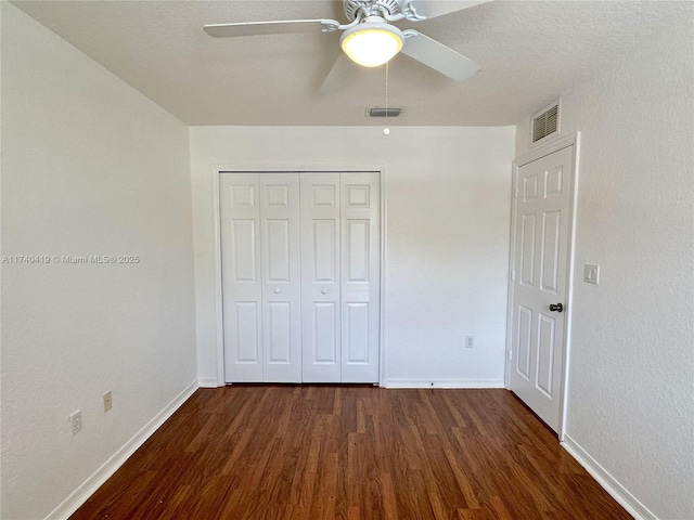 unfurnished bedroom featuring dark wood-type flooring, a closet, baseboards, and visible vents