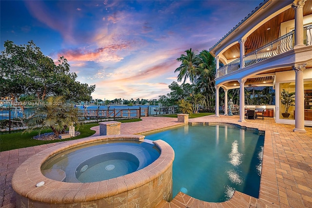 pool at dusk featuring an in ground hot tub and a patio