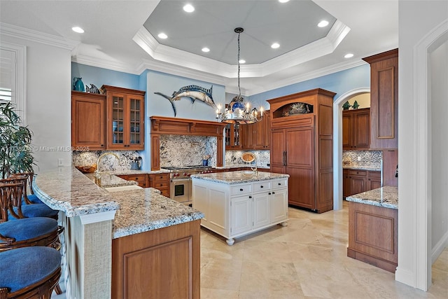 kitchen with a kitchen bar, sink, double oven range, a raised ceiling, and kitchen peninsula