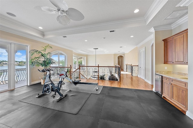 exercise room featuring ornamental molding, ceiling fan, a tray ceiling, a water view, and a textured ceiling