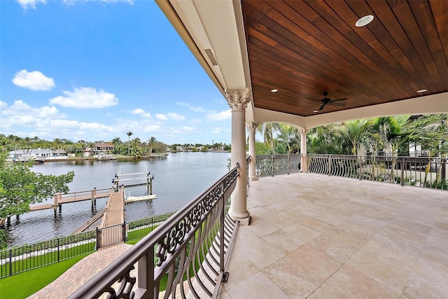 view of patio with a water view, a dock, and ceiling fan