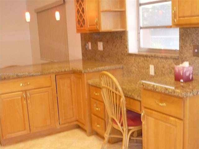 kitchen featuring built in desk, decorative backsplash, hanging light fixtures, light tile patterned floors, and light stone counters